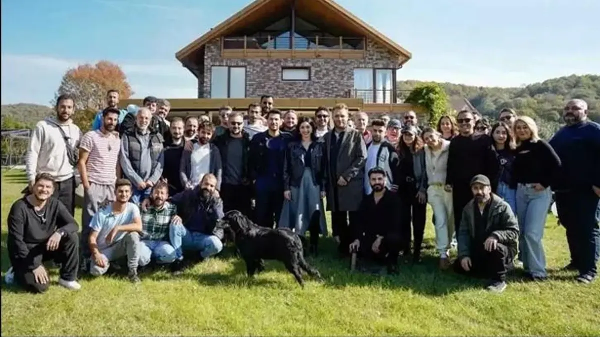 Oyuncu kadrosunun setteki neşeli bir anını gösteren toplu set fotoğrafı.